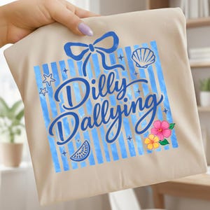 Könnte beinhalten: Beige Tragetasche mit blauem Design. Das Design umfasst eine Schleife, einen gestreiften Hintergrund und die Worte "Dilly Dallying". Es zeigt auch eine Muschel, Sterne, eine Wassermelonen-Scheibe und tropische Blumen.