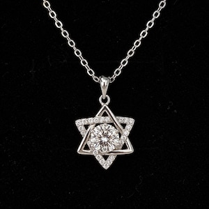 May include: A silver-toned necklace featuring a Star of David pendant. The pendant is crafted with a central round brilliant-cut stone surrounded by smaller pavé-set stones along the star frame, suspended from a delicate link chain.