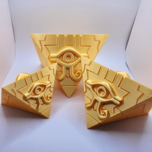 May include: Three yellow, triangular objects featuring an eye symbol. The largest is a pyramid shape, and the other two are smaller triangles. The eye symbol is in the centre of each object, with detailed design.