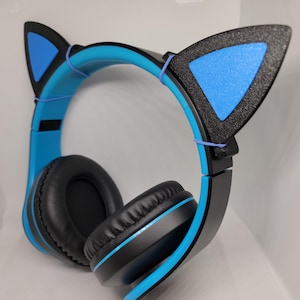 May include: Blue and black cat ear headphones. The headphones feature a blue headband and ear cups, with black ear pads. The cat ears are black with blue centres. The headphones are designed for over-the-ear use.