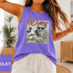 Peut inclure: Un d&eacute;bardeur violet sans manches avec une impression graphique en noir et blanc de Walt Disney et Mickey Mouse. Le mot Walt est imprim&eacute; dans une grande police rouge stylis&eacute;e au-dessus de l'image. Le d&eacute;bardeur a une encolure ronde.