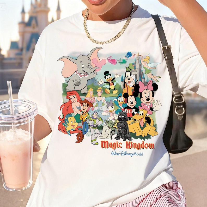 K&ouml;nnte beinhalten: Wei&szlig;es T-Shirt mit einem farbenfrohen Aufdruck von Disney-Figuren wie Dumbo, Mickey Mouse und Minnie Mouse. Der Text "Magic Kingdom Walt Disney World" ist darunter gedruckt. Das T-Shirt hat einen klassischen Rundhalsausschnitt.