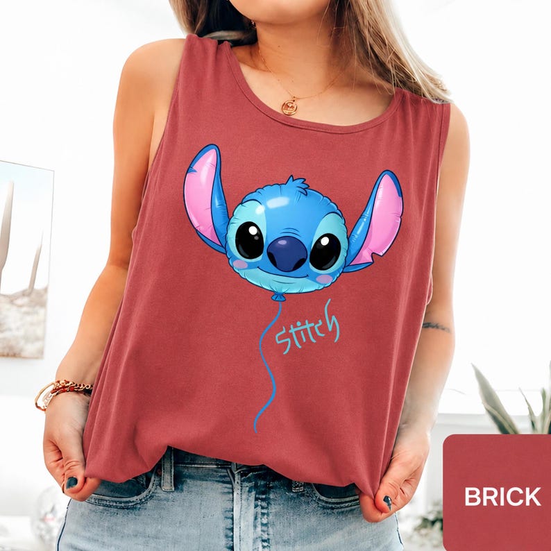 May include: A brick red sleeveless tank top featuring a graphic of a blue Stitch character shaped like a balloon with large ears and black eyes. Below the balloon, the word Stitch is printed in a light blue script font with a dangling string.