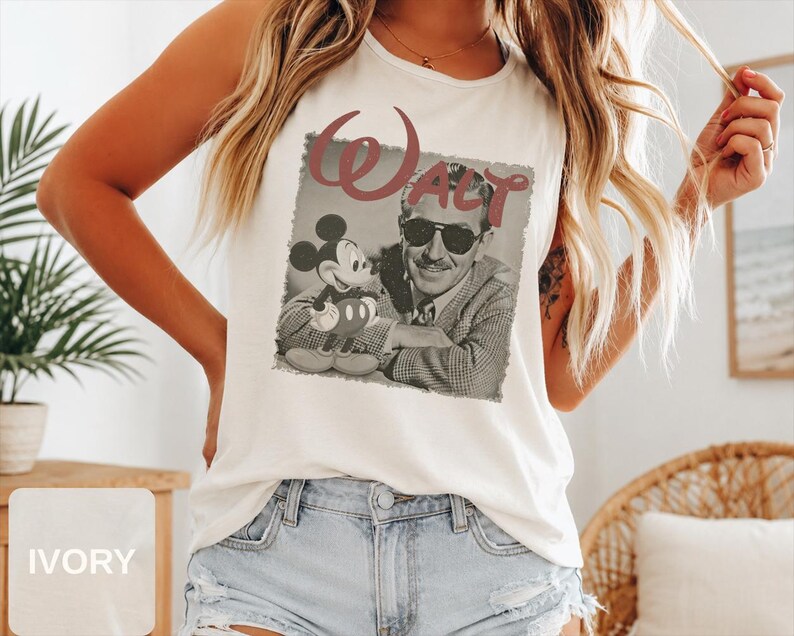 Peut inclure: Un d&eacute;bardeur sans manches ivoire avec une impression graphique de style vintage repr&eacute;sentant Walt Disney et Mickey Mouse. L'image en noir et blanc montre Walt Disney portant des lunettes de soleil et une veste &agrave; motifs, avec le mot WALT en grandes lettres rouges au-dessus.