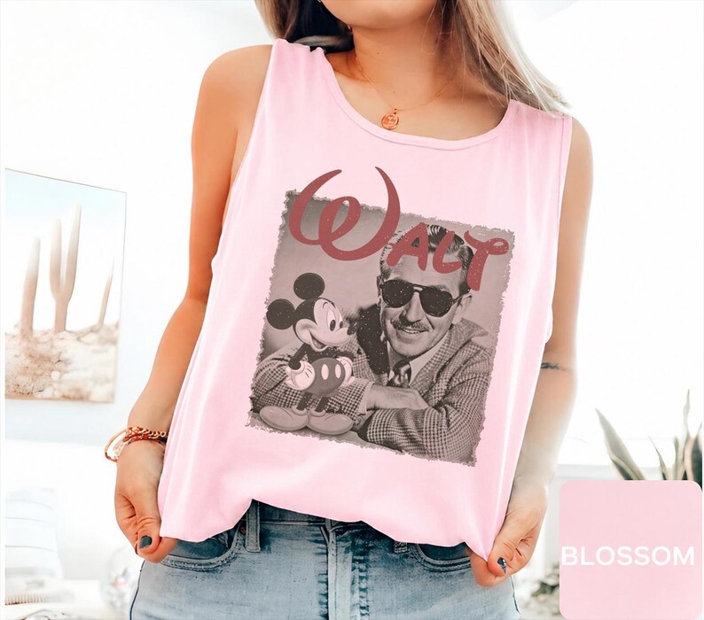 Peut inclure: Un d&eacute;bardeur rose clair sans manches avec une impression graphique de Walt Disney portant des lunettes de soleil &agrave; c&ocirc;t&eacute; de Mickey Mouse. Le mot Walt est imprim&eacute; dans une police rouge fonc&eacute; stylis&eacute;e au-dessus de l'image photographique en noir et blanc.