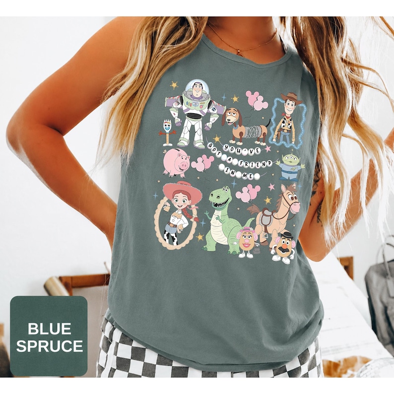 May include: A blue spruce sleeveless shirt featuring a graphic print of Toy Story characters including Buzz Lightyear, Woody, Jessie, Rex, Slinky Dog, Hamm, and the Aliens. The text "YOU'VE GOT A FRIEND IN ME" is printed in the center with pink balloons.