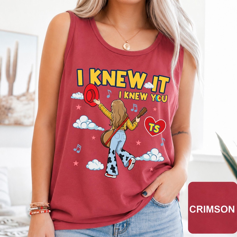 May include: A crimson sleeveless tank top featuring a graphic illustration of a person with long hair holding a guitar and a red hat. The text reads I KNEW IT I KNEW YOU with a heart containing the letters TS, surrounded by clouds, stars, and music notes.