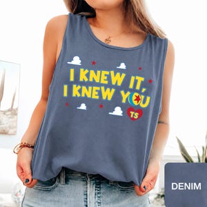 May include: A denim blue sleeveless tank top featuring the yellow text I KNEW IT, I KNEW YOU with a colourful ball icon, a red heart with the letters TS, and small white cloud and red star graphics printed across the front chest area.