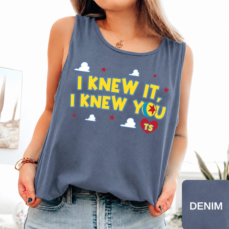 May include: A denim blue sleeveless tank top featuring the yellow text I KNEW IT, I KNEW YOU with a colourful ball icon, a red heart with the letters TS, and small white cloud and red star graphics printed across the front chest area.