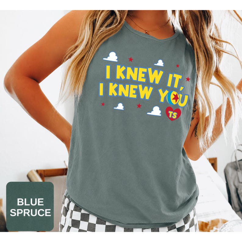 May include: A blue spruce sleeveless tank top featuring the yellow text I KNEW IT, I KNEW YOU with a colourful ball graphic, a red heart with the letters TS, and small white cloud and red star accents printed on the front of the garment.
