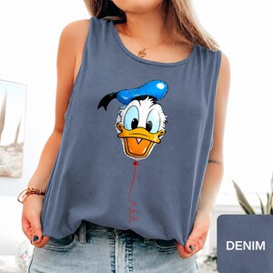 Op de afbeelding: Een leiblauwe mouwloze tanktop met een grafische print van het gezicht van Donald Duck, ontworpen als een blauw-witte ballon met een rood touwtje dat naar beneden hangt. Het shirt heeft een ronde halslijn en een relaxte pasvorm van zachte stof.