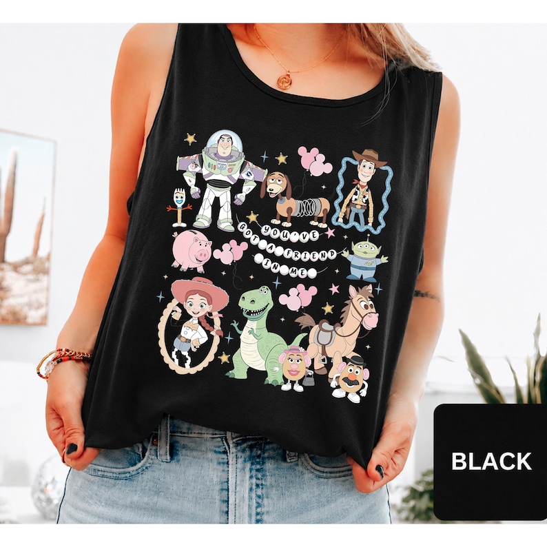 May include: A black sleeveless tank top featuring a colorful graphic print of various animated characters including a space ranger, a cowboy, a cowgirl, a dinosaur, a pig, and a dog. The text "YOU'VE GOT A FRIEND IN ME" is printed in the center.