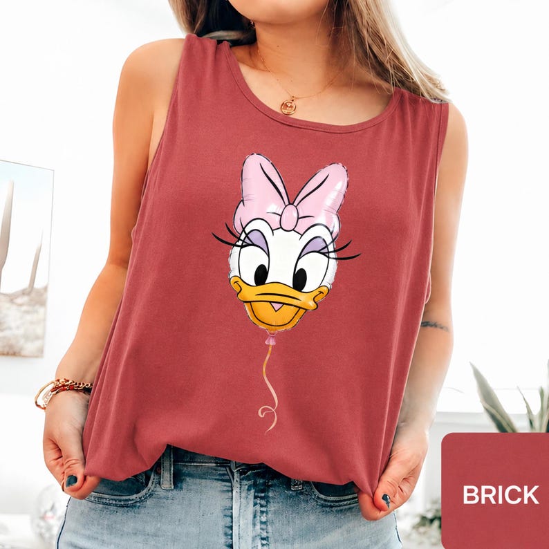 Op de afbeelding: Een baksteenrood mouwloos hemdje met een grafische print van het gezicht van Daisy Duck, gestileerd als een roze ballon met een touwtje. Het personage heeft een grote roze strik, lange wimpers en een gele snavel. Het shirt heeft een ronde hals.