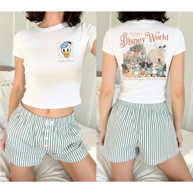 May include: White t-shirt with a Donald Duck graphic and the text "Custom Name". The back of the shirt features a Disney World graphic. Paired with green and white striped shorts.