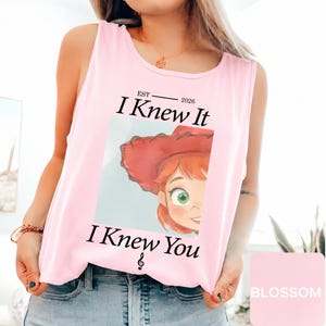 May include: A light pink sleeveless tank top featuring a graphic print of a cartoon character with red hair and a red hat. The text reads "EST 2026 I Knew It I Knew You" with a small musical treble clef symbol centered below the text.