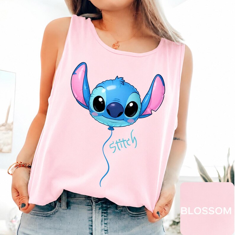 May include: A light pink sleeveless tank top featuring a graphic of a blue character shaped like a balloon with large black eyes and pink inner ears. Below the balloon, the word Stitch is written in a light blue cursive script font.