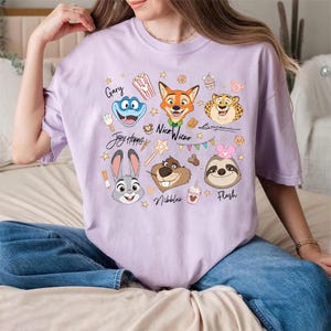 Pu&ograve; includere: Una maglietta lilla chiaro con personaggi dei cartoni animati di Zootropolis. Il design include Judy Hopps, Nick Wilde, Flash e altri personaggi, insieme ai nomi Gary, Benjamin e Nibbles. La maglietta ha un girocollo e maniche corte.