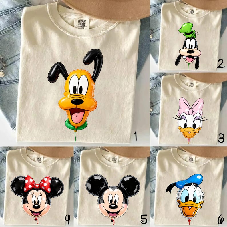 May include: A collection of six cream-colored t-shirts, each featuring a different Disney character designed as a balloon. The characters include Pluto, Goofy, Daisy Duck, Minnie Mouse, Mickey Mouse, and Donald Duck, all with a small green string.