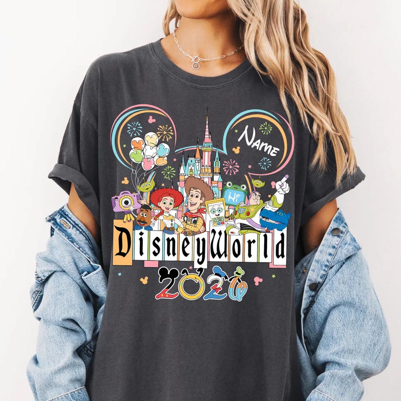 Peut inclure: T-shirt gris fonc&eacute; avec un motif color&eacute; de Disney World. Le design comprend des personnages Disney, un ch&acirc;teau, des feux d'artifice et les mots "Disneyworld 2020". Le t-shirt a des manches retrouss&eacute;es et une coupe d&eacute;contract&eacute;e.