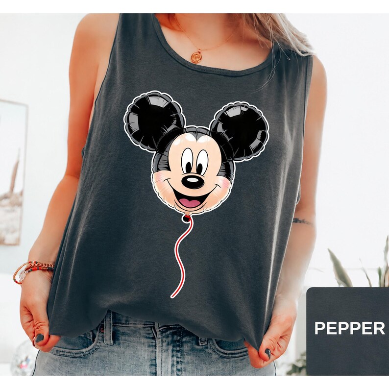 Op de afbeelding: Een donkergrijs mouwloos hemd met een grafische print van een Mickey Mouse-hoofd in de vorm van een zwarte ballon met een witte omlijning en een rood touwtje. Het shirt heeft een ronde hals en wordt gedragen met een blauwe spijkerbroek.