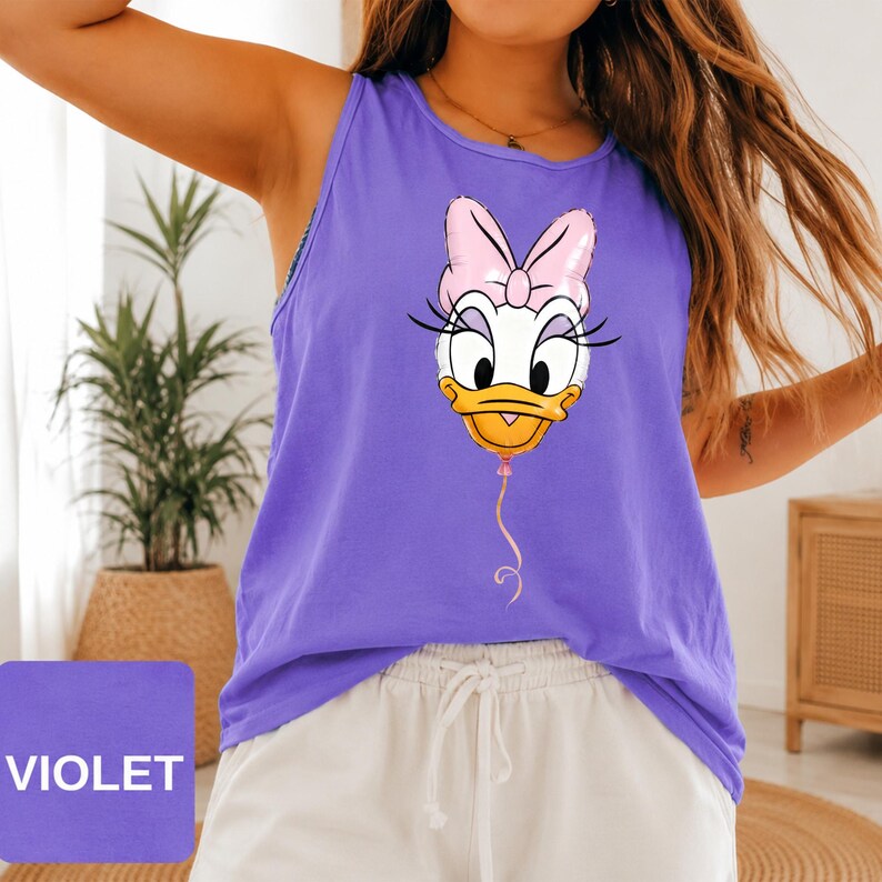 Op de afbeelding: Een violet mouwloos hemdje met een grafische print van een wit eendfiguur met een gele snavel en een roze strik, ontworpen als een ballon met een touwtje dat vanaf de kin naar beneden hangt. De top heeft een ronde halslijn.