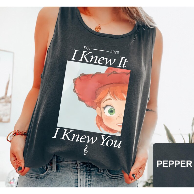 May include: A charcoal gray sleeveless tank top featuring a graphic print of a cartoon character with red hair and a red hat. The text reads "EST 2026 I Knew It I Knew You" with a small musical treble clef symbol below the text.