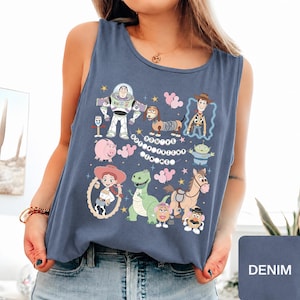 May include: A slate blue sleeveless tank top featuring a graphic print of various Toy Story characters including Buzz Lightyear, Woody, Jessie, Rex, Slinky Dog, and others, with the text "YOU'VE GOT A FRIEND IN ME" arranged in a circular pattern.