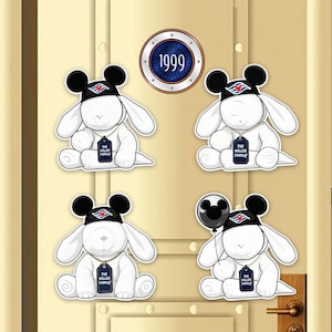 May include: Four white plush bunny figures wearing black Mickey Mouse hats and holding tags that read "THE MILLER FAMILY." One bunny holds a black Mickey Mouse balloon. A circular emblem displays "1999."