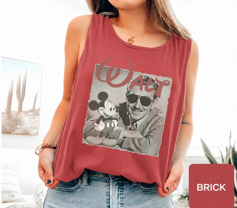 Peut inclure: Un d&eacute;bardeur sans manches rouge brique avec une impression graphique en noir et blanc de Walt Disney et Mickey Mouse. Le mot Walt est imprim&eacute; dans une grande police stylis&eacute;e au-dessus des personnages. Le d&eacute;bardeur a une encolure ronde.