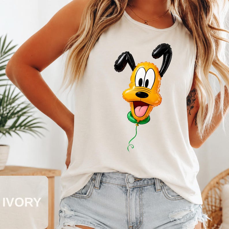Op de afbeelding: Een ivoorkleurige mouwloze tanktop met een grafische print van een gele hond die is ontworpen als een glanzende ballon. Het personage heeft zwarte oren, een zwarte neus en een groene ballonknoop aan de onderkant met een dun groen touwtje.