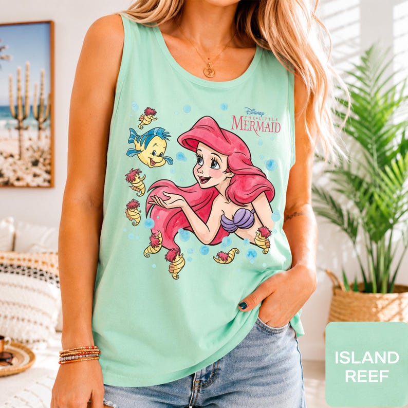 Peut inclure: Un d&eacute;bardeur sans manches vert clair avec une impression graphique d'Ariel de La Petite Sir&egrave;ne, ses cheveux rouges, son haut coquillage violet et le personnage Polochon, entour&eacute;s de petits hippocampes et de bulles bleues avec le logo Disney.
