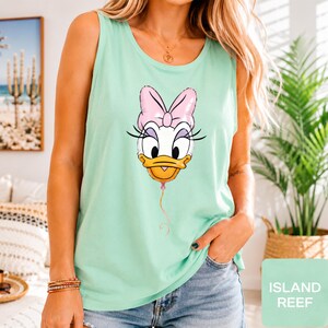 Op de afbeelding: Een licht mintgroene mouwloze tanktop met een grafische print van het gezicht van Daisy Duck, gestileerd als een roze ballon met een dun touwtje naar beneden. Het personage heeft een grote roze strik, lange wimpers en een gele snavel.