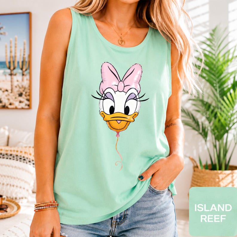 Op de afbeelding: Een licht mintgroene mouwloze tanktop met een grafische print van het gezicht van Daisy Duck, gestileerd als een roze ballon met een dun touwtje naar beneden. Het personage heeft een grote roze strik, lange wimpers en een gele snavel.
