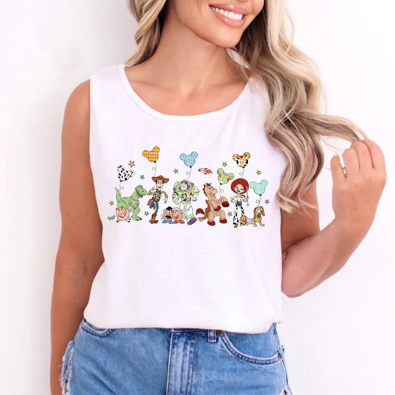 May include: White tank top featuring a colorful graphic of cartoon characters with balloons. The design includes a dinosaur, cowboy, space ranger, horse, and cowgirl. The tank top is sleeveless and made of a soft material.