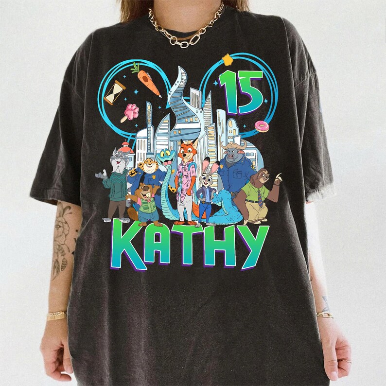 May include: Dark gray t-shirt featuring a colorful graphic of characters from the movie Zootopia, with the number 15 and the name KATHY. The design includes a cityscape and various food items. The shirt has a vintage, worn look.
