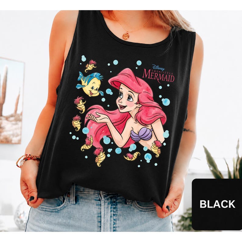 Peut inclure: Un d&eacute;bardeur noir sans manches avec une impression graphique d'Ariel de La Petite Sir&egrave;ne aux cheveux rouges, un haut coquillage violet et son ami Polochon. Le motif inclut des petits hippocampes jaunes, des bulles bleues et le texte Disney The Little Mermaid.