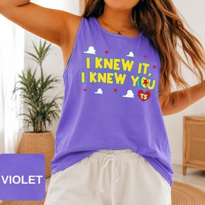 May include: A violet sleeveless tank top featuring the yellow text I KNEW IT, I KNEW YOU with a colourful ball graphic, a red heart containing the letters TS, and small white cloud and red star icons printed across the front of the garment.