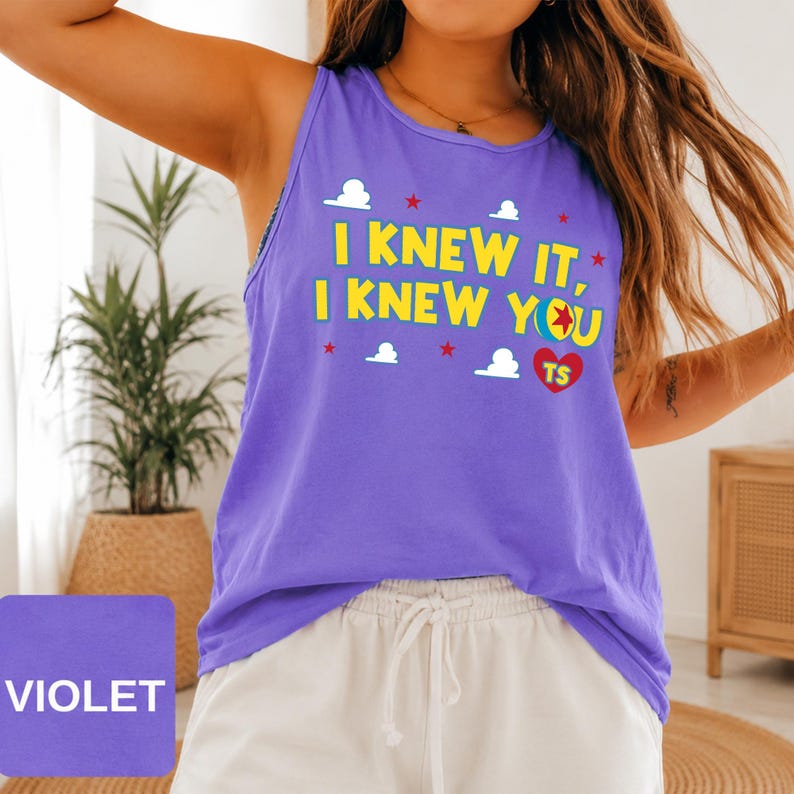 May include: A violet sleeveless tank top featuring the yellow text I KNEW IT, I KNEW YOU with a colourful ball graphic, a red heart containing the letters TS, and small white cloud and red star icons printed across the front of the garment.