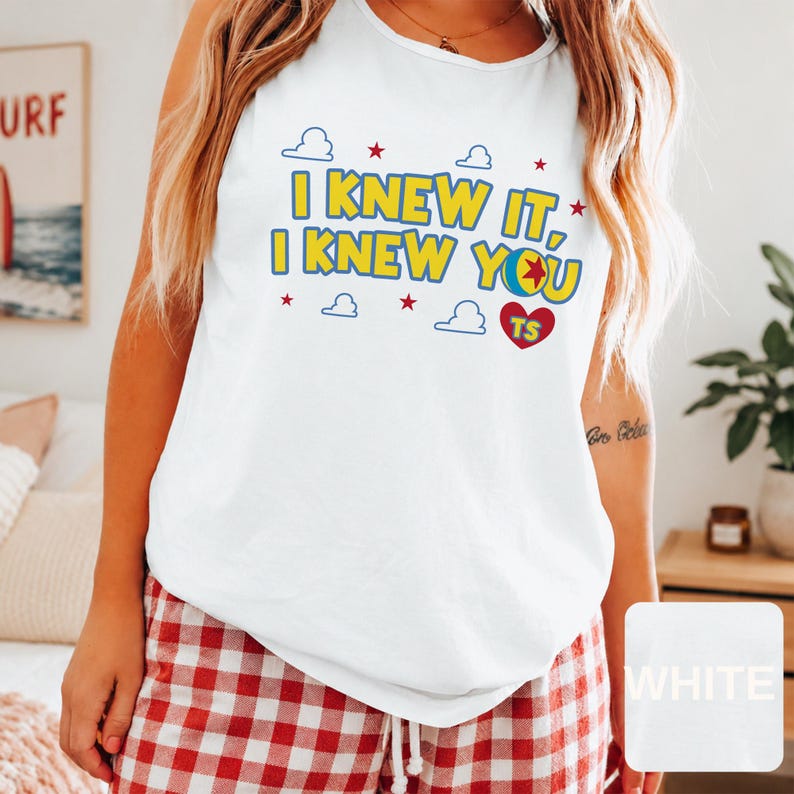 May include: A white sleeveless tank top featuring the yellow text I KNEW IT, I KNEW YOU with a colourful ball graphic replacing the letter O, a red heart with the letters TS, and small blue cloud and red star graphics printed on the front.