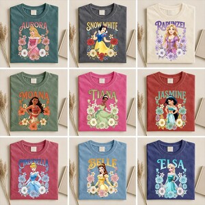 Puede incluir: Nueve camisetas coloridas con princesas de Disney. Cada camiseta muestra el nombre y la imagen de una princesa rodeada de dise&ntilde;os florales. Las camisetas son de varios colores, incluyendo verde azulado, gris, beige, verde, rosa, rojo y azul.