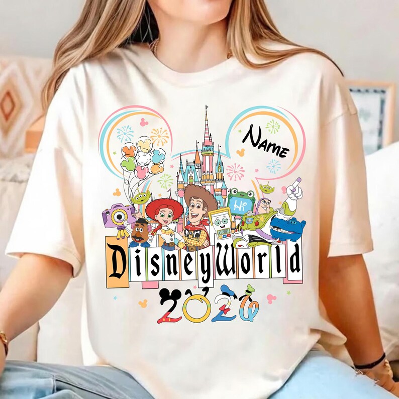 Peut inclure: T-shirt cr&egrave;me avec un graphisme color&eacute; de Disney World. Le motif comprend le ch&acirc;teau de Disney World, divers personnages de dessins anim&eacute;s et le texte "Disneyworld 2020". Un "Nom" personnalisable est &eacute;galement inclus.