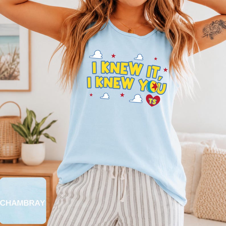 May include: A light blue sleeveless tank top featuring the yellow text I KNEW IT, I KNEW YOU with a colourful ball graphic, small white clouds, red stars, and a red heart containing the letters TS printed on the front of the garment.
