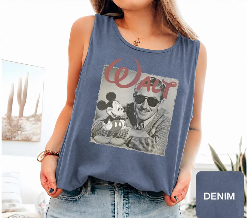 Peut inclure: Un d&eacute;bardeur bleu denim sans manches avec une impression graphique en noir et blanc de Walt Disney et Mickey Mouse, accompagn&eacute;e du mot Walt en grandes lettres cursives roses au-dessus de l'image carr&eacute;e. Le d&eacute;bardeur a une encolure ronde.
