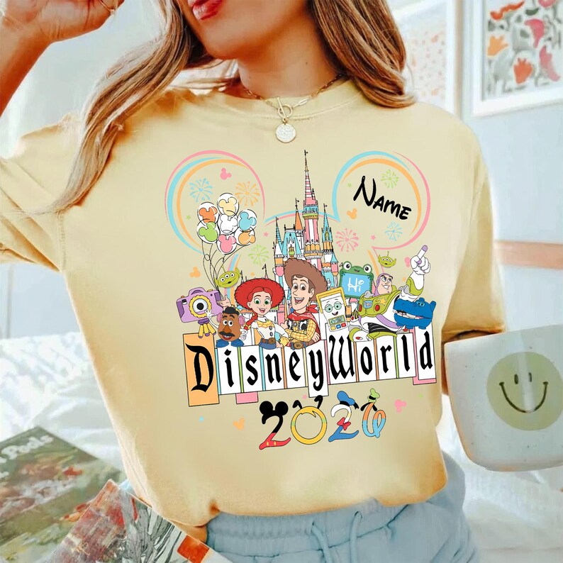 Peut inclure: T-shirt jaune clair avec un motif Disney World color&eacute;. Le motif comprend un ch&acirc;teau, des personnages et le texte "Disneyworld 2020". Un espace est pr&eacute;vu pour un nom personnalis&eacute;.