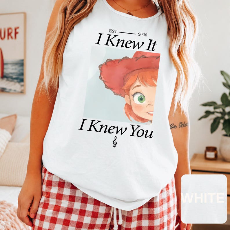 May include: A white sleeveless tank top featuring a graphic print of a cartoon character with red hair and a red hat. The text reads "EST 2026 I Knew It I Knew You" with a small musical note symbol below the text, centered on the front of the garment.