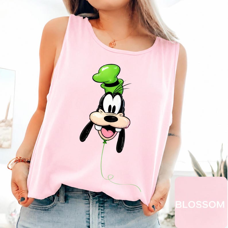 Op de afbeelding: Een lichtroze mouwloos hemdje met een grafische print van het personage Goofy, ontworpen als een groene ballon met een touwtje dat naar beneden loopt. Het personage heeft een zwarte neus, witte ogen en een groene hoed, gecentreerd op de borst.