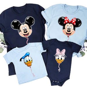 May include: A collection of four garments including a navy blue t-shirt with a Mickey Mouse balloon graphic, a light blue t-shirt with a Minnie Mouse balloon graphic, a light blue t-shirt with a Donald Duck balloon, and a navy blue baby bodysuit.