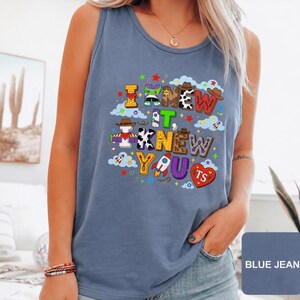 Może przedstawiać: Niebieski tank top w kolorze jeansu z kolorowym nadrukiem graficznym z napisem I KNEW IT, KNEW YOU. Wz&oacute;r zawiera r&oacute;żne motywy, takie jak łaty krowie, elementy kosmiczne i kowbojskie kapelusze, przeplatane małymi gwiazdkami, chmurami i rakietami.