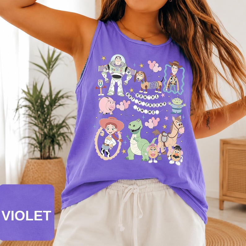 May include: A violet tank top featuring a graphic print of various Toy Story characters including Buzz Lightyear, Woody, Jessie, Rex, and Slinky Dog, with the text "YOU'VE GOT A FRIEND IN ME" arranged in a circular pattern among pink balloons.
