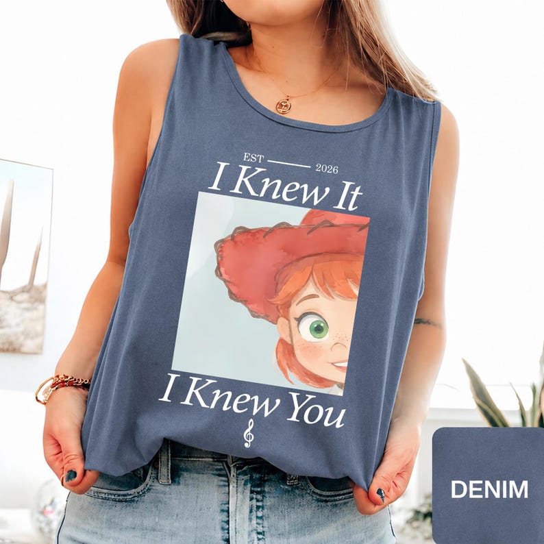 May include: A slate blue sleeveless tank top featuring a graphic print of a cartoon character with red hair and a red hat. The text reads EST 2026 I Knew It I Knew You with a treble clef symbol below the text. The design is centered on the chest.
